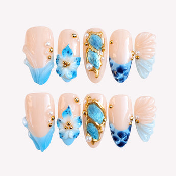 Couronne de Sirène mermaid seashell press on nails with a nude and blush-pink base, aqua-blue accents, raised shell-like 3D details, gold-tone framing and a medium almond shape.