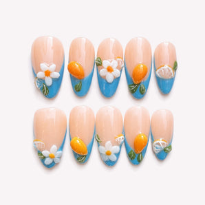 Capri Escape blue French tip nails with flowers, a nude-blush base, sculptural citrus accents, green leaves and a medium almond shape.