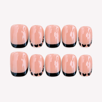 Little Crush short black French tip nails with tiny hearts on a warm nude base.