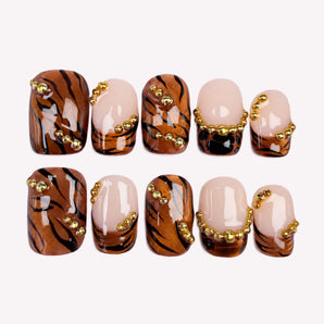 Copper Instinct brown chrome nails with tiger stripes, nude French tips, and gold-tone bead accents.
