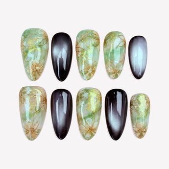 Moonlit Meadow green chrome nails with gold-tone flower outlines and black cat eye accents.