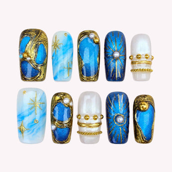 Starlit Treasure press on nails with luminous blue panels, gold-tone frames and pearl-like accents.