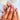 Seashell Garden coastal nails worn on a hand in a medium almond shape with sculptural shell details, white floral motifs, layered French tips and gold-tone accents.