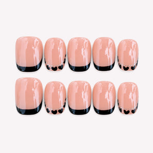 Little Crush short black French tip nails with tiny hearts on a warm nude base.