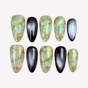 Moonlit Meadow green chrome nails with gold-tone flower outlines and black cat eye accents.